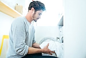 Man at home doing laundry, putting clothes in the washing machine.